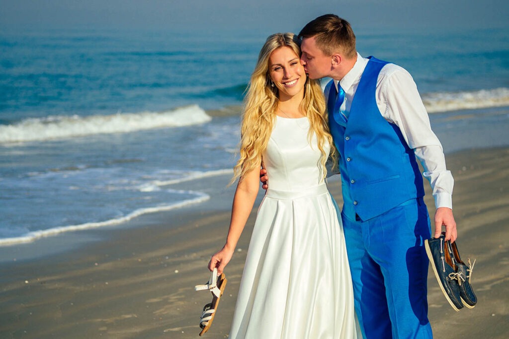 Ein hübscher Bräutigam in einem schicken Anzug küsst eine schöne Braut in einem Hochzeitskleid am Strand auf der Insel Ruegen