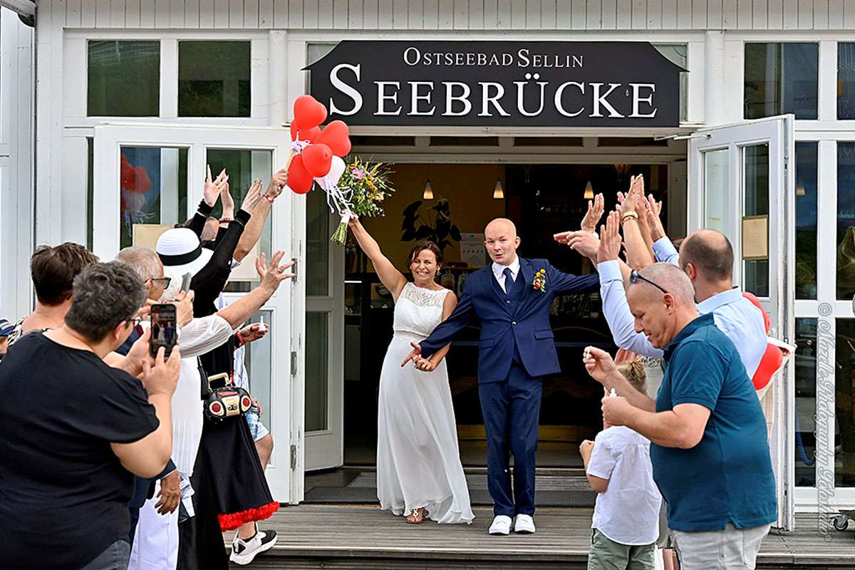 Das frisch vermählte Hochzeitspaar verlässt den historischen Trausaal der Seebrücke Sellin und wird von Familie und Freunden im liebevoll gestalteten Spalier empfangen. Die Ostsee im Hintergrund, das Lichtspiel auf dem Wasser und die emotionale Atmosphäre machen diesen Moment einzigartig. Fotografisch begleitet vom Hochzeitsfotografen des Mazelle Photography Fotostudio® – mit Feingefühl und künstlerischem Blick eingefangen.