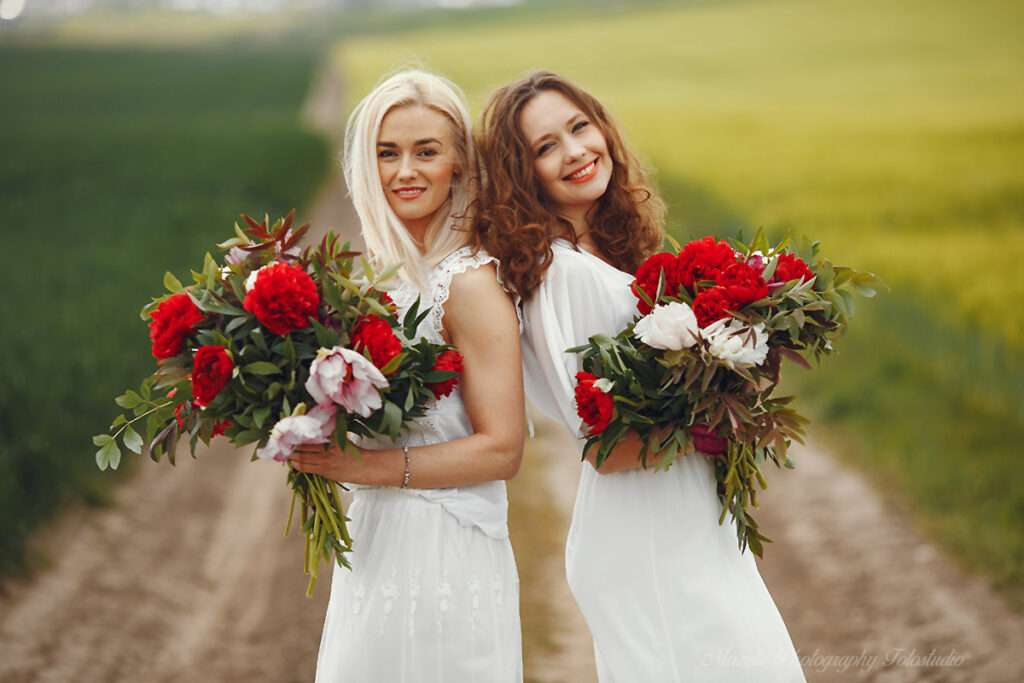 Mazelle Photography Fotostudio® begleitet eine LGBTQ‑Hochzeit auf Rügen: Zwei Frauen stehen Rücken an Rücken auf der Wiese im weißen Hochzeitskleid und halten den Brautstrauß. Voller Freude und Verbundenheit wird dieser emotionale Moment authentisch und professionell festgehalten – eine Hochzeitsfotografie, die über Rügen hinaus auch internationale Paare aus Polen und Europa anspricht.