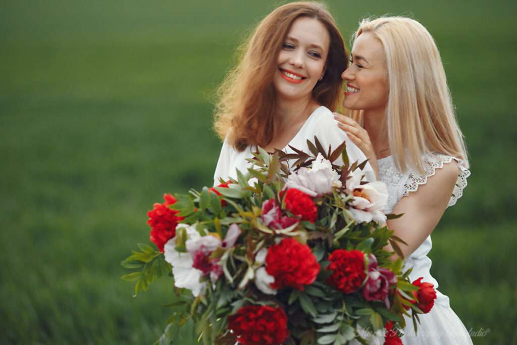 Mazelle Photography Fotostudio® begleitet eine LGBTQ‑Hochzeit auf Rügen: Zwei Frauen stehen Rücken an Rücken auf der Wiese im weißen Hochzeitskleid und halten den Brautstrauß. Voller Freude und Verbundenheit wird dieser emotionale Moment authentisch und professionell festgehalten – eine Hochzeitsfotografie, die über Rügen hinaus auch internationale Paare aus Polen und Europa anspricht.