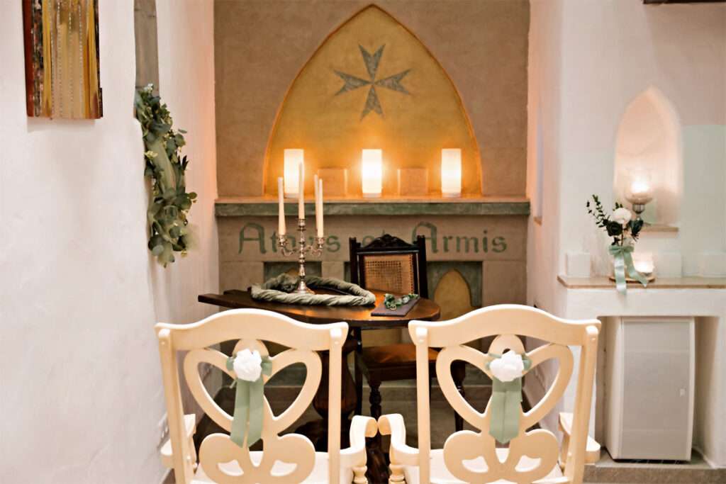 In der festlich geschmückten Ordenskapelle Binz stehen die beiden Stühle bereit, auf denen das Brautpaar während der Trauung vor dem Altar Platz nimmt. Diese liebevoll arrangierte Szene unterstreicht die besondere Atmosphäre der Zeremonie und verleiht den Hochzeitsfotos eine authentische und emotionale Note. Der hochzeitsfotograf des mazelle photography fotostudio® aus dranske auf rügen hält diesen Moment stilvoll fest und schafft Erinnerungen voller Eleganz und Bedeutung.