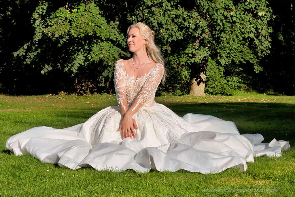 Im Schlosspark des Schlosses Hohendorf sitzt die Braut in ihrem Hochzeitskleid auf dem grünen Rasen – wie eine Prinzessin. Mit strahlendem Lächeln zeigt sie ihren Ehering nach der Vermählung. In dieser romantischen Kulisse entstehen besonders schöne Hochzeitsfotos, die vom hochzeitsfotograf des mazelle photography fotostudio® aus dranske auf rügen aufgenommen wurden. Die Kombination aus historischer Architektur, natürlicher Umgebung und emotionaler Nähe macht diese Aufnahmen zu einzigartigen Erinnerungen voller Eleganz und Authentizität.