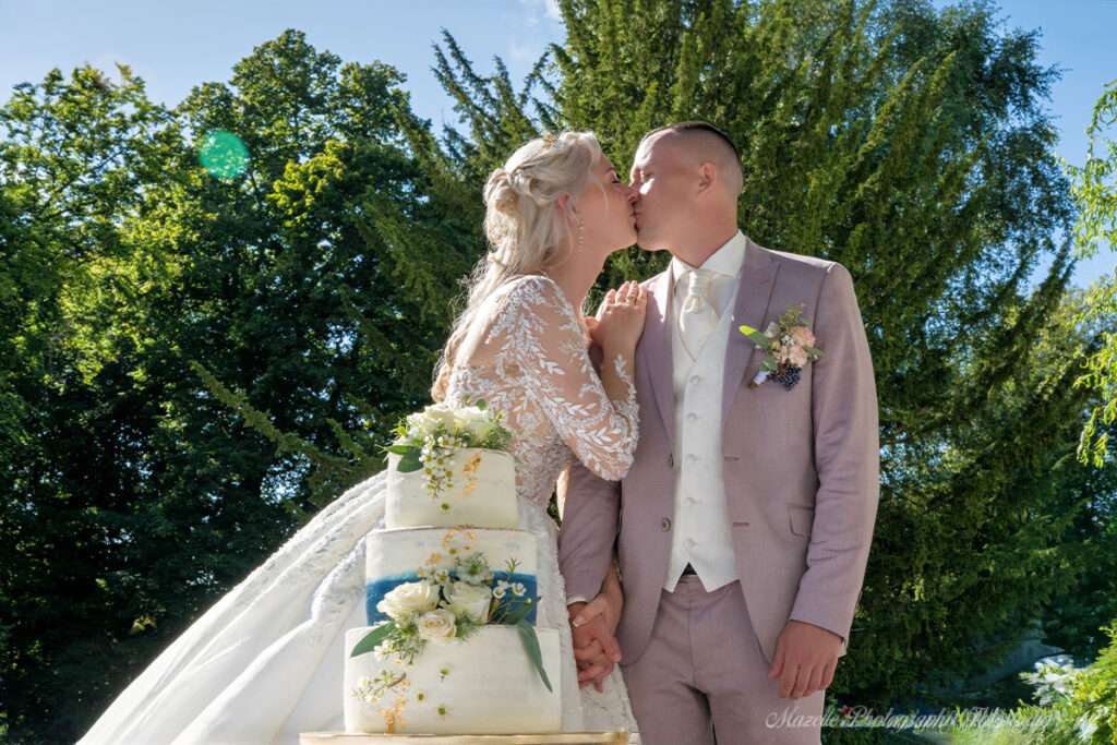 Das Brautpaar steht vor der festlich dekorierten Hochzeitstorte im Schloss Hohendorf und gibt sich einen liebevollen Kuss, bevor sie gemeinsam die Torte anschneiden. Dieser intime Moment voller Romantik und Freude wird fotografisch begleitet vom mazelle photography fotostudio® von rügen. Die Hochzeitsfotografie verbindet Authentizität, Eleganz und emotionale Tiefe und macht die Erinnerung an diesen besonderen Augenblick unvergänglich.