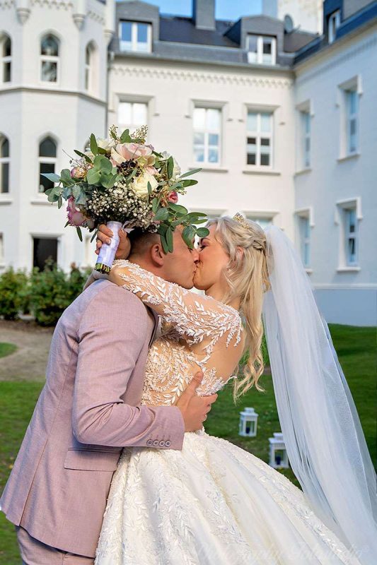 Die Braut hält ihren Brautstrauß in der Hand und wird liebevoll vom Bräutigam geküsst – ein inniger Moment direkt nach der Trauung im Schloss Hohendorf. Der Hochzeitsfotograf des mazelle photography fotostudio® von rügen durfte diese besondere Szene festhalten. Die historische Kulisse des Schlosses und die romantische Atmosphäre verleihen den Hochzeitsfotos Eleganz und Authentizität. So entstehen Bilder, die nicht nur den Augenblick dokumentieren, sondern die Liebe und Verbundenheit des Brautpaars für immer sichtbar machen.